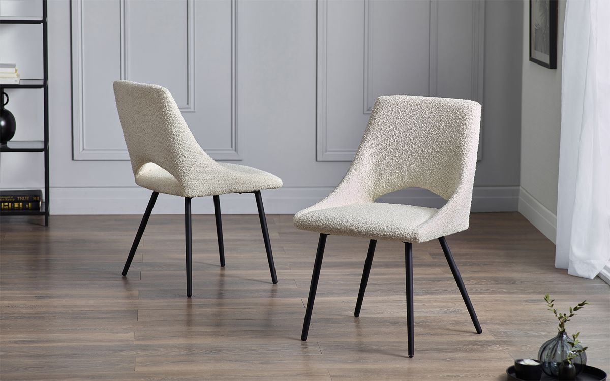 Two ivory boucle dining chairs with black legs and comfortable seat pads, placed in a room with a modern design.